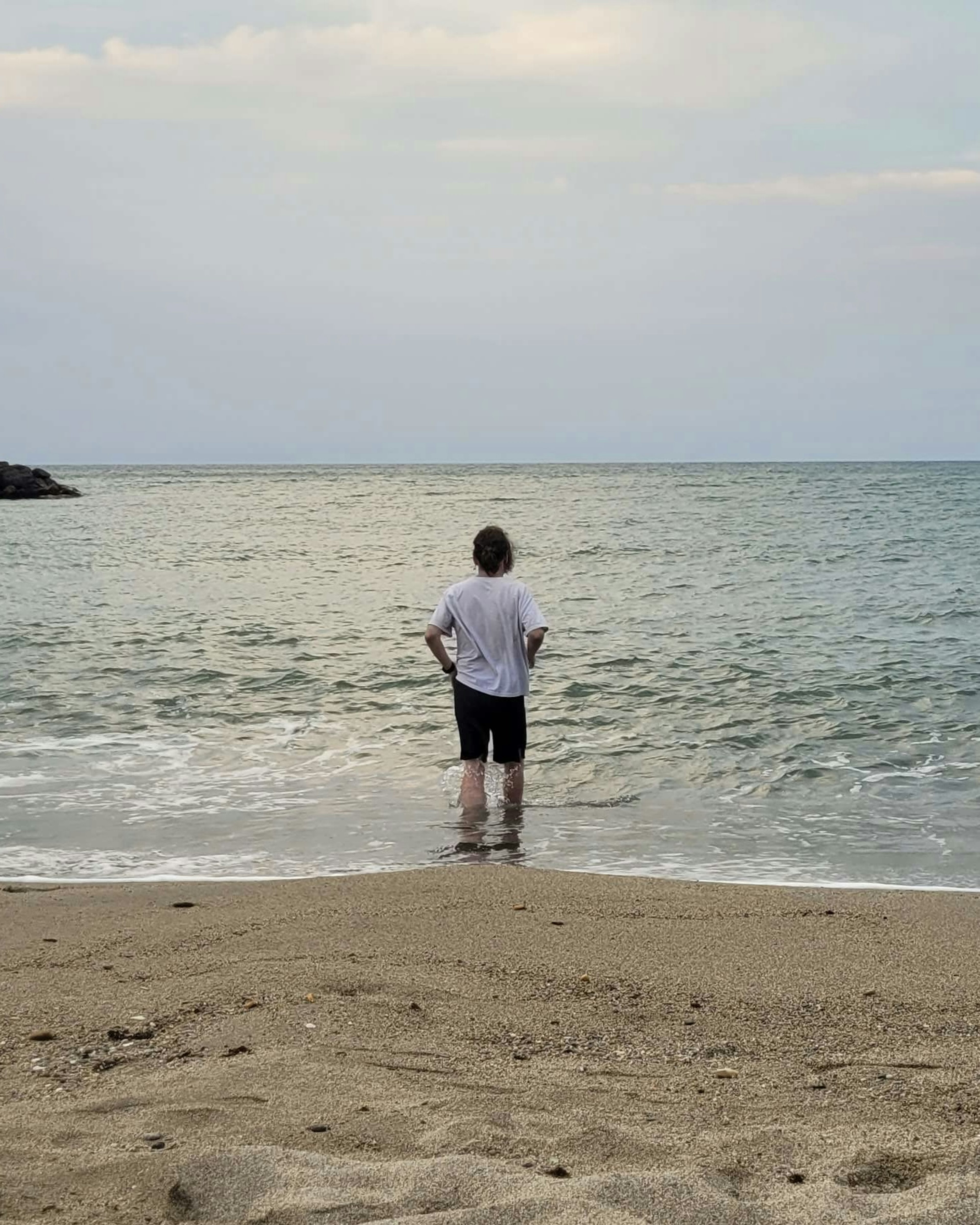 Picture of myself wearing a black short and a white t-shirt, walking into the sea, knee-deep in water